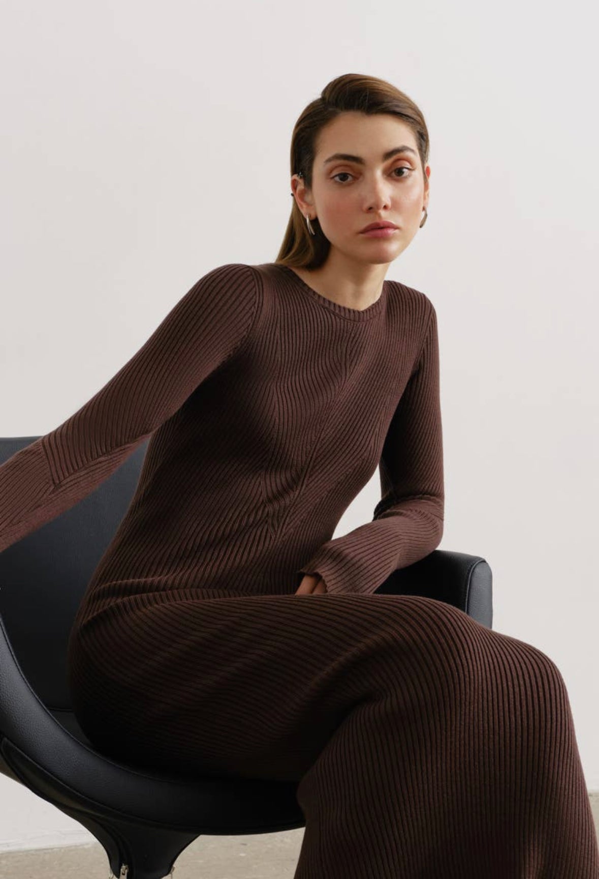 A chocolate-colored long-sleeved knit with a flattering regular fit, designed to accentuate your waist and complemented by a pencil-shaped skirt. The garment features a round neck, fine ribbed design, and falls neatly at a midi length.