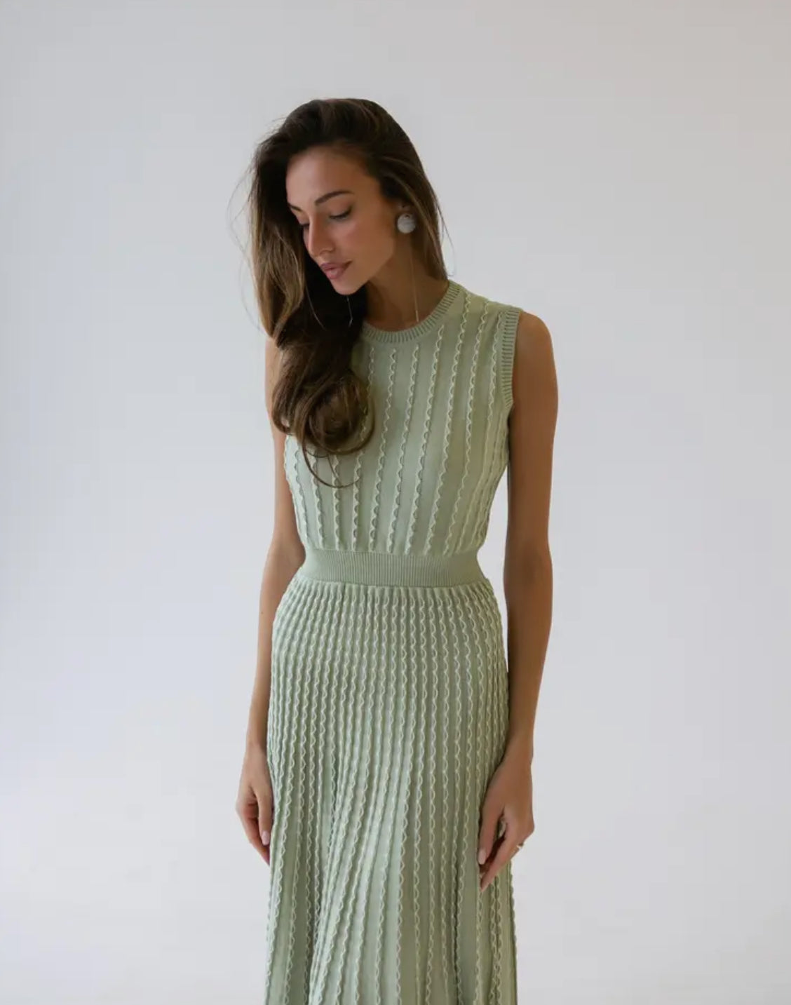 A feminine, soft, and airy dress in olive, designed to emphasize the body figure with a sleeveless, round neck style, falling below the knee.