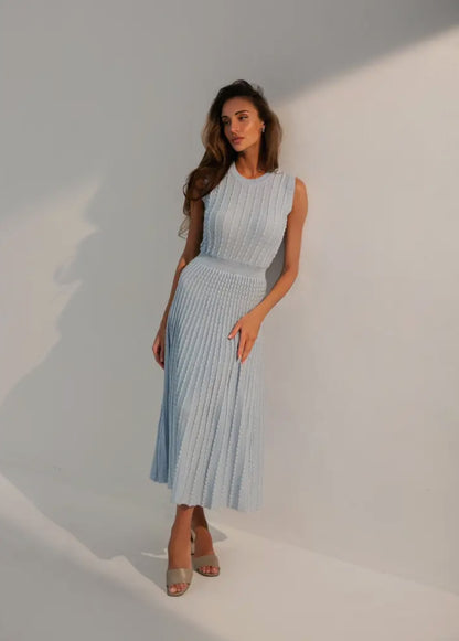 A feminine, soft, and airy dress in blue, designed to emphasize the body figure with a sleeveless, round neck style, falling below the knee.