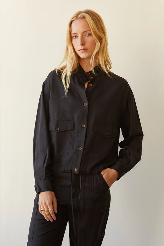 A lightweight tencel blend jacket with a fabric composition of 57% rayon, 20% tencel, 18% cotton, and 5% linen. Features include a mock neck, front button closure, two front flap pockets with button closure, cuff button closure, and drawstring bottom hem. Model is wearing size small.