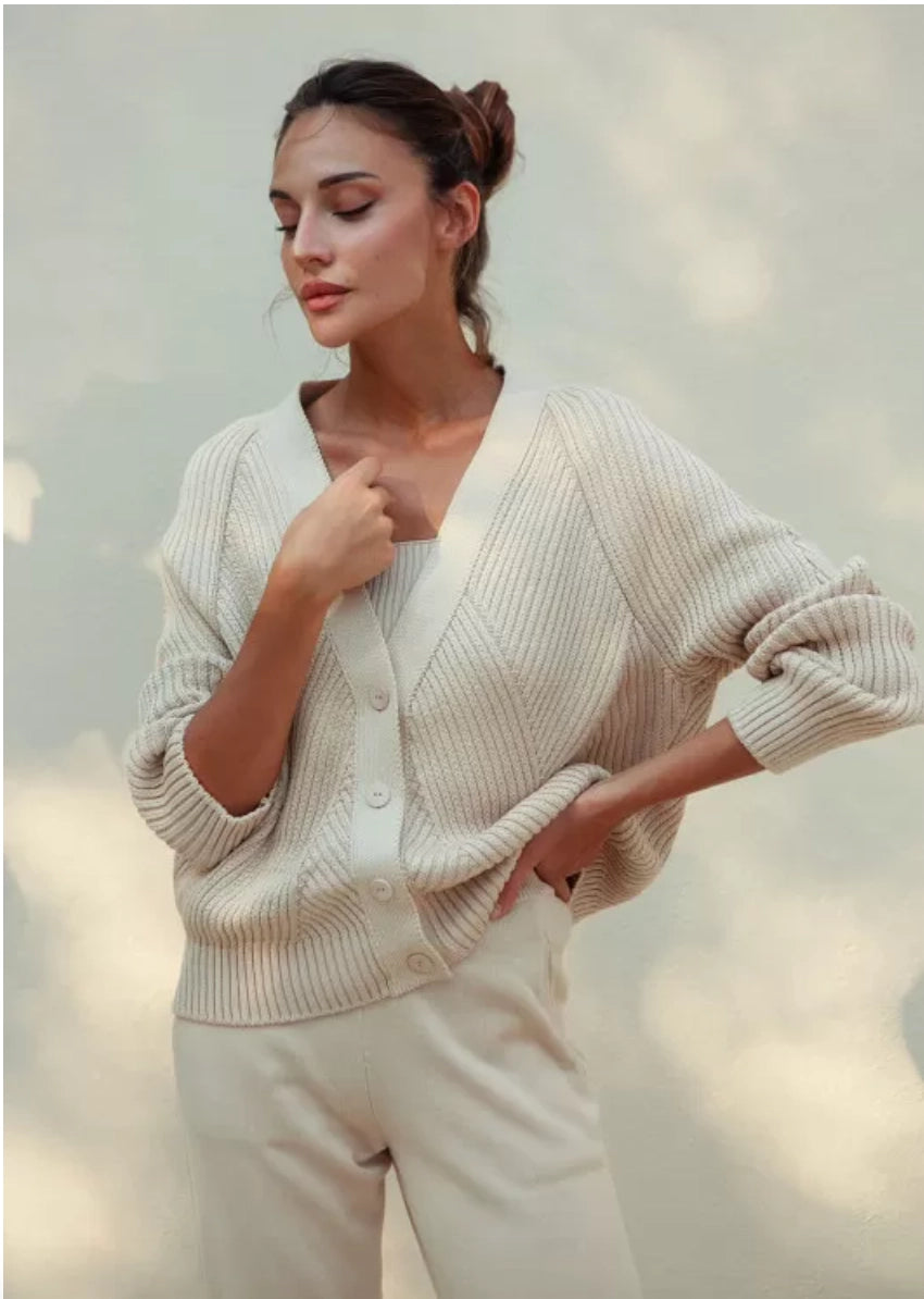 A cream-colored, knitted cotton-rich cardigan with a relaxed fit, V-neckline, and classic button closure.