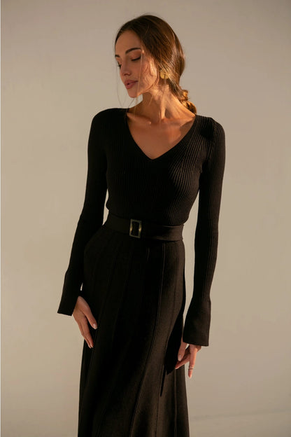 A feminine dress with a plunging neckline and waist belt, falling below the knee with long sleeves for a comfortable fit that emphasizes the body figure.